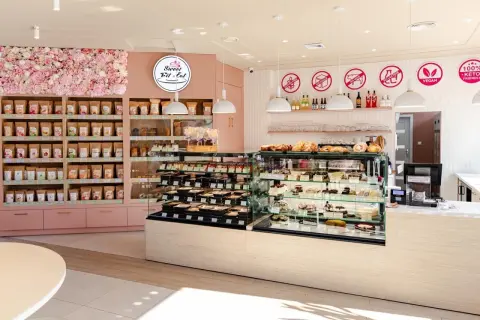 Wnętrze cukierni "Sweet Fit & Eat" z witrynami pełnymi ciast i ciasteczek. Reklama cukierni podkreśla opcje bez glutenu, cukru i laktozy.