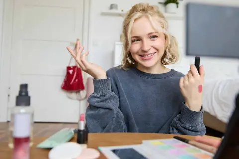 Uśmiechnięta influencerka z pomadką na dłoni pokazuje, jak zostać ambasadorem marki, nagrywając tutorial makijażowy.