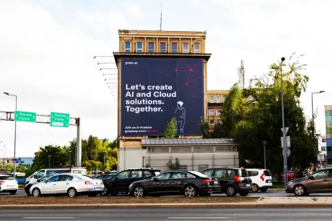 Na wielkiej reklamie z dominującymi **kolorami analogicznymi** – granatem i czerwienią – widnieje hasło "Let's create AI and Cloud solutions. Together.". W tle ruchliwa ulica z samochodami.