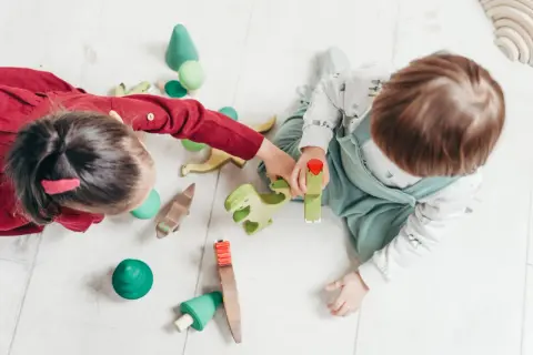 Dzieci bawią się drewnianymi zabawkami, tworząc scenkę z dinozaurami. Idealne reklamy zabawek dla małych odkrywców.
