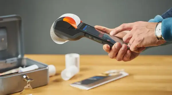 Ręce obsługują kasę fiskalną z rolką paragonu. To kluczowy element visual marketing, ułatwiający transakcje.