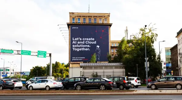 Na wielkiej reklamie z dominującymi **kolorami analogicznymi** – granatem i czerwienią – widnieje hasło "Let's create AI and Cloud solutions. Together.". W tle ruchliwa ulica z samochodami.