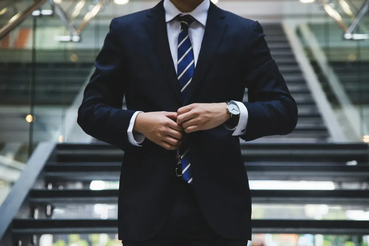 Elegancki mężczyzna w garniturze, z pewnością jako brand ambassador, zapina marynarkę na schodach.