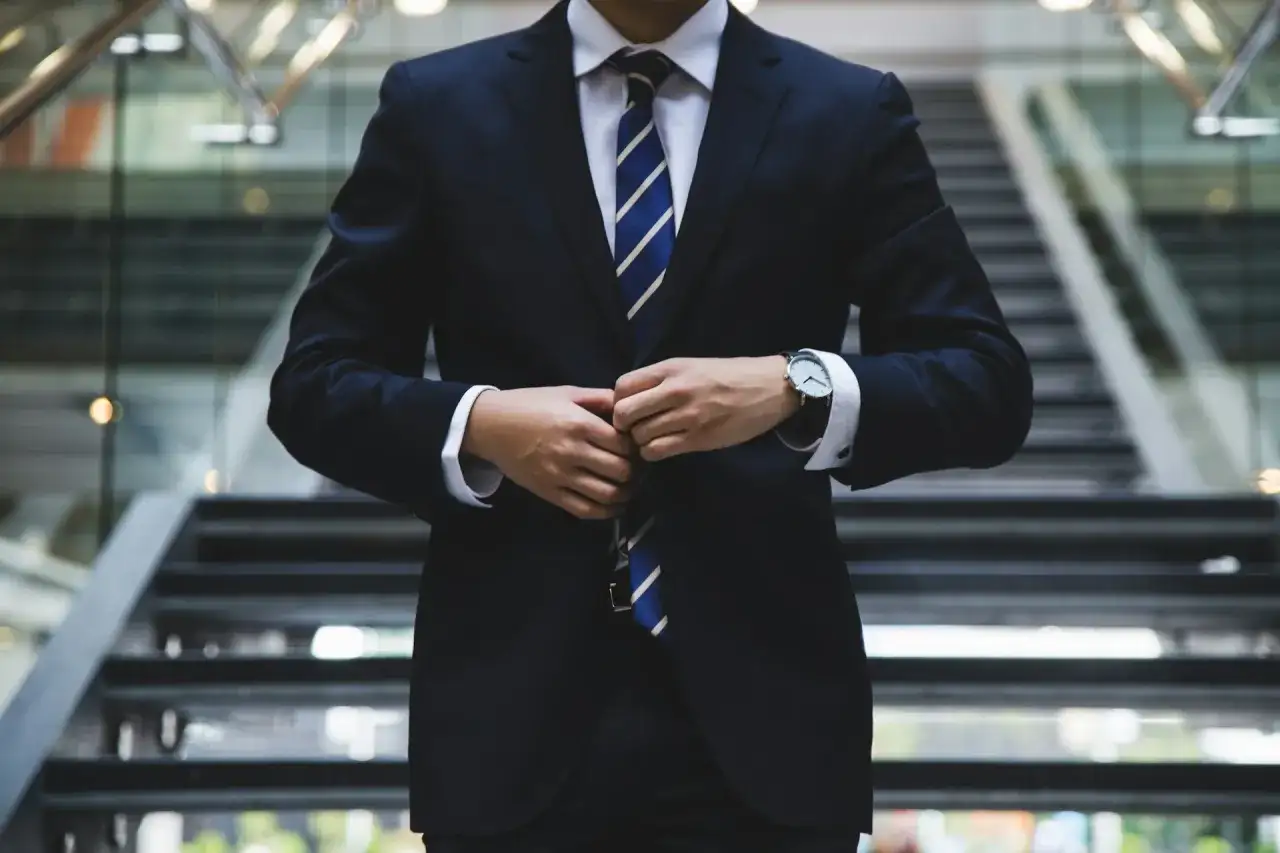 Elegancki mężczyzna w garniturze, z pewnością jako brand ambassador, zapina marynarkę na schodach.
