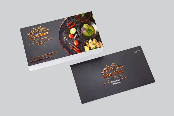 Wizytówki restauracji Red Hot Chilli Pepper z lśniącym, miedzianym logo i zdjęciem potrawy. To przykład, co to jest laminat – nadaje elegancji i trwałości.