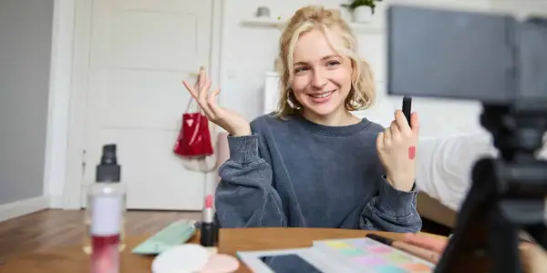 Uśmiechnięta influencerka z pomadką na dłoni pokazuje, jak zostać ambasadorem marki, nagrywając tutorial makijażowy.