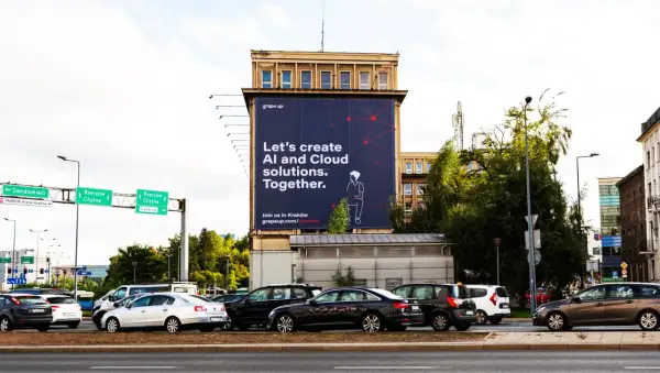 Na wielkiej reklamie z dominującymi **kolorami analogicznymi** – granatem i czerwienią – widnieje hasło "Let's create AI and Cloud solutions. Together.". W tle ruchliwa ulica z samochodami.