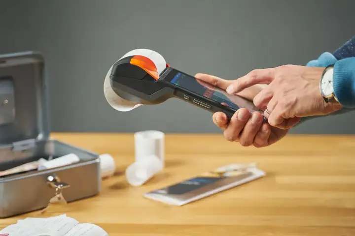 Ręce obsługują kasę fiskalną z rolką paragonu. To kluczowy element visual marketing, ułatwiający transakcje.